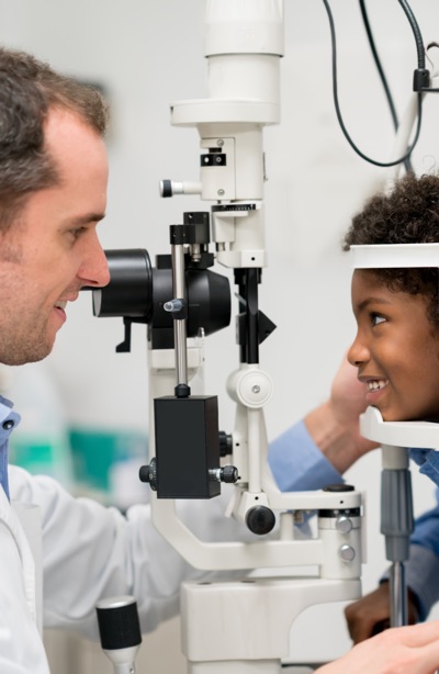 Happy African American boy getting an eye exam at the optician on the phoropter - medical concepts