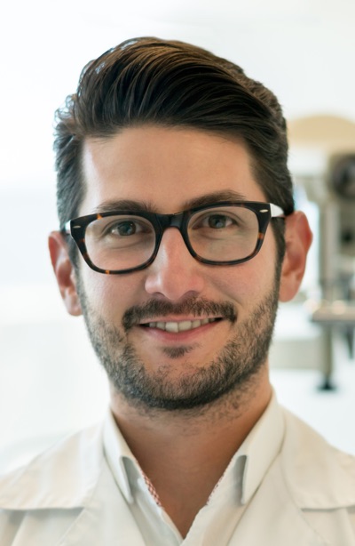 Portrait of male opthalmologist looking at camera smiling and a phoropter at the background - Focus on foreground